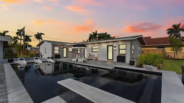 back of property at dusk featuring a fenced in pool, a patio area, fence, and stucco siding