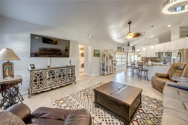 tiled living room with lofted ceiling, stacked washer and clothes dryer, and ceiling fan