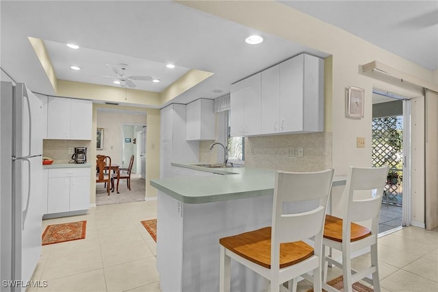 kitchen with a tray ceiling, refrigerator, sink, white cabinets, and kitchen peninsula