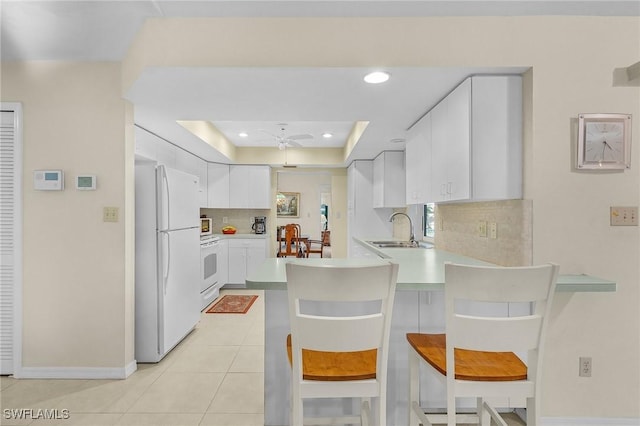 kitchen with sink, a breakfast bar area, kitchen peninsula, a raised ceiling, and white appliances