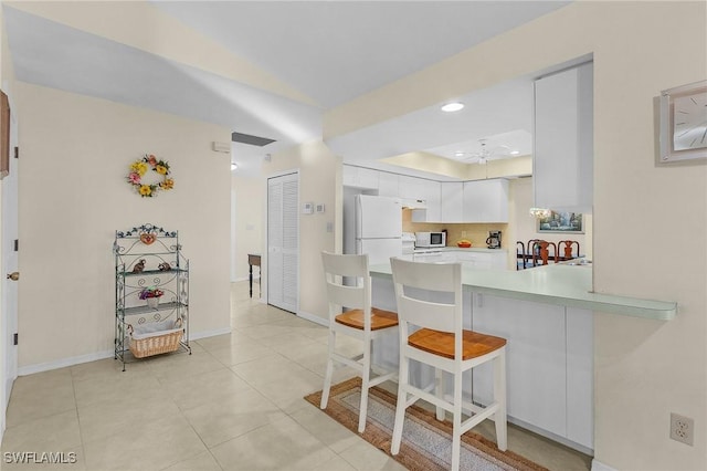 kitchen featuring white cabinets, a kitchen bar, light tile patterned flooring, kitchen peninsula, and white fridge