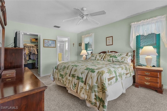 carpeted bedroom with connected bathroom, a walk in closet, a closet, and ceiling fan