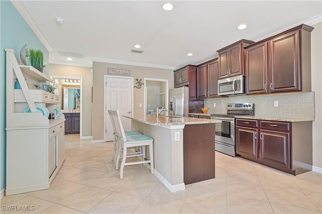 kitchen featuring a breakfast bar area, ornamental molding, stainless steel appliances, a kitchen island with sink, and decorative backsplash