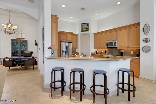 kitchen featuring a breakfast bar, backsplash, kitchen peninsula, stainless steel appliances, and light stone countertops