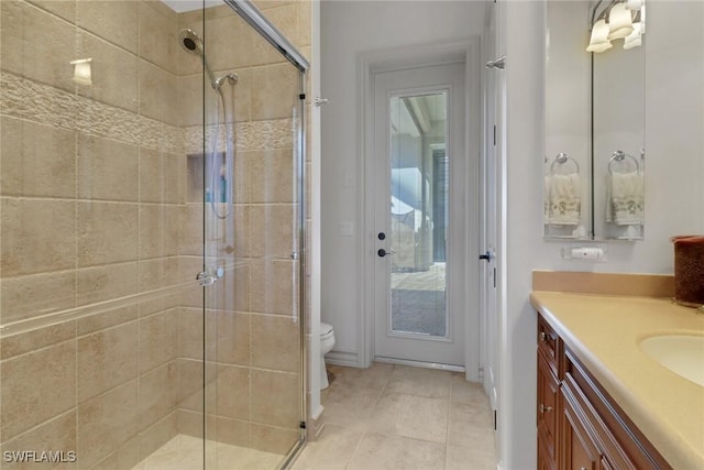 bathroom with a shower with door, vanity, tile patterned floors, and toilet