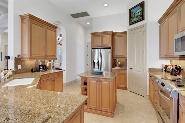 kitchen featuring appliances with stainless steel finishes, sink, hanging light fixtures, a center island, and light stone counters