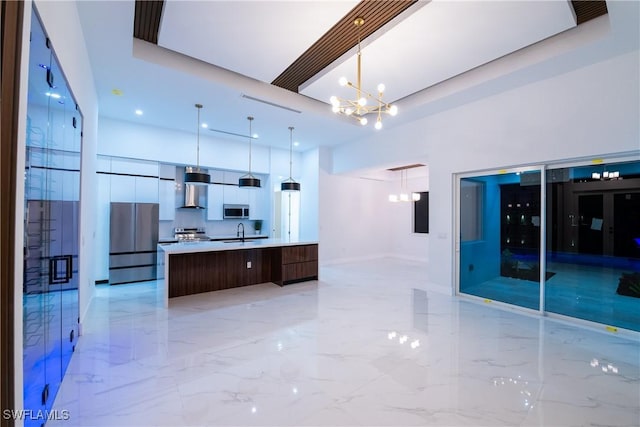 kitchen featuring sink, wall chimney range hood, appliances with stainless steel finishes, decorative light fixtures, and a large island with sink