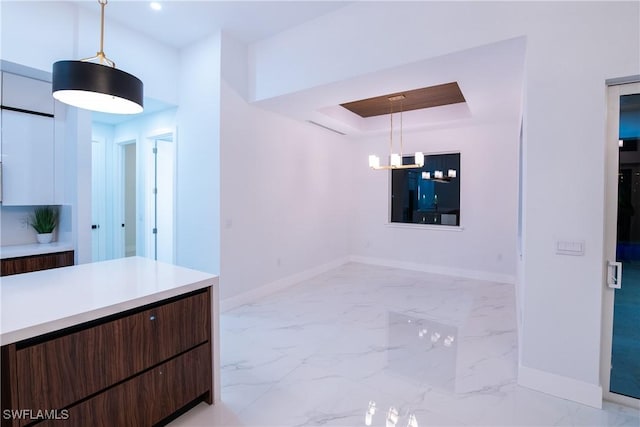 kitchen with a tray ceiling, a notable chandelier, decorative light fixtures, and dark brown cabinets