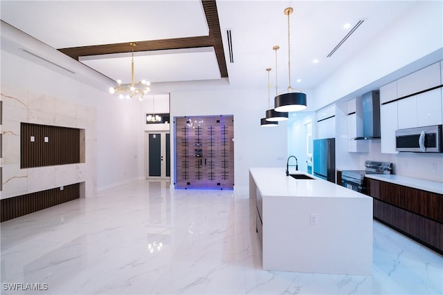 kitchen with decorative light fixtures, appliances with stainless steel finishes, wall chimney exhaust hood, and a center island with sink