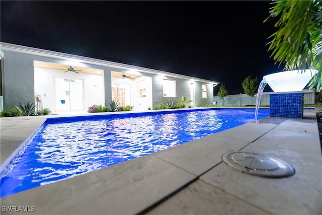 pool at twilight featuring pool water feature, a patio, and ceiling fan