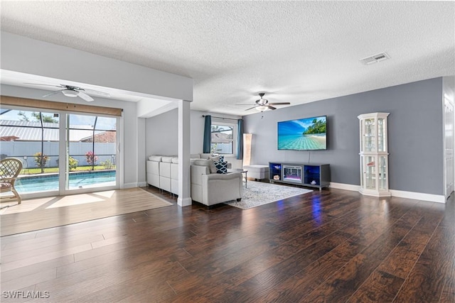 living room with ceiling fan, plenty of natural light, dark hardwood / wood-style floors, and a textured ceiling