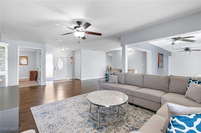 living room featuring dark wood-type flooring, ceiling fan, and a textured ceiling