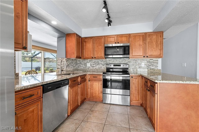 kitchen with appliances with stainless steel finishes, sink, light stone counters, and kitchen peninsula