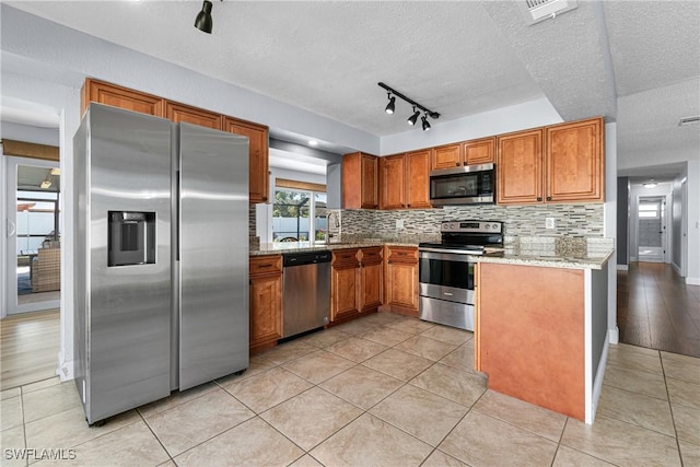 kitchen with tasteful backsplash, light stone countertops, appliances with stainless steel finishes, and light tile patterned floors