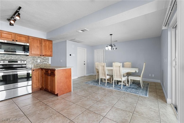 kitchen with pendant lighting, backsplash, stainless steel appliances, light stone counters, and light tile patterned flooring