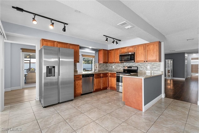 kitchen with light tile patterned floors, stainless steel appliances, light stone counters, tasteful backsplash, and a textured ceiling