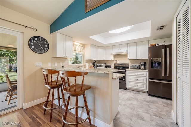 kitchen featuring a breakfast bar area, a raised ceiling, kitchen peninsula, stainless steel appliances, and white cabinets