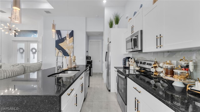 kitchen with appliances with stainless steel finishes, pendant lighting, sink, dark stone countertops, and white cabinets