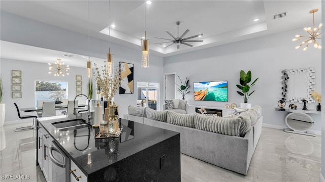 living room with ceiling fan with notable chandelier, a tray ceiling, sink, and a high ceiling