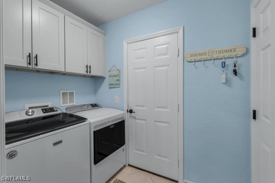 laundry area featuring washing machine and dryer, cabinets, and light tile patterned flooring