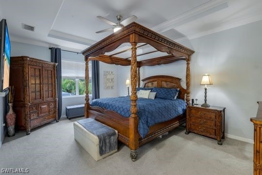 bedroom featuring light carpet, a tray ceiling, crown molding, and ceiling fan