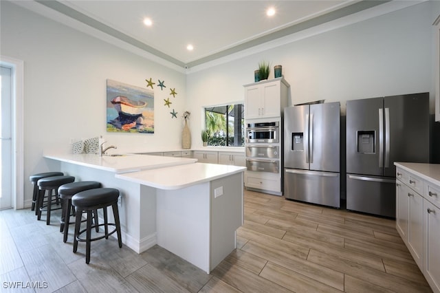 kitchen with sink, a breakfast bar, appliances with stainless steel finishes, white cabinets, and kitchen peninsula