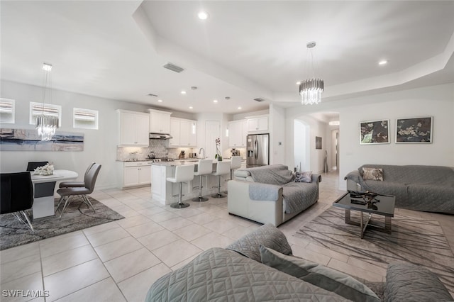 tiled living room featuring a tray ceiling and a notable chandelier