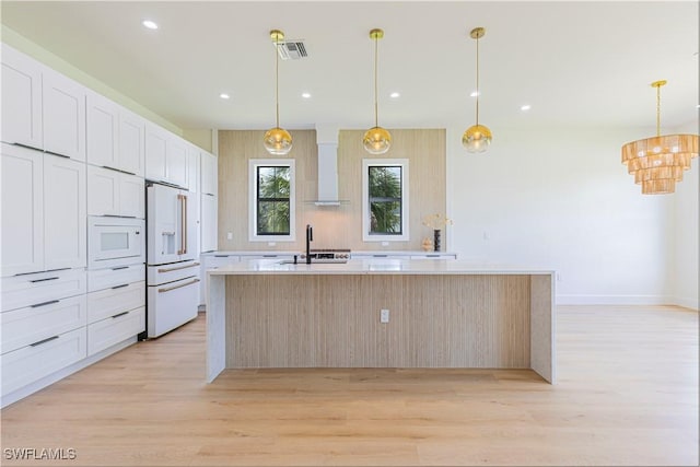 kitchen with an island with sink, pendant lighting, white cabinets, and white appliances