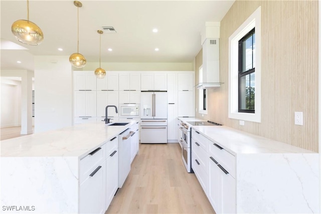 kitchen with pendant lighting, high quality appliances, white cabinetry, sink, and wall chimney range hood