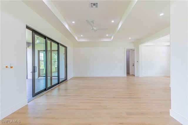 unfurnished room featuring ceiling fan, a raised ceiling, and light wood-type flooring