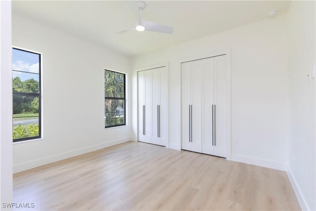 unfurnished bedroom featuring multiple windows, two closets, light hardwood / wood-style flooring, and ceiling fan