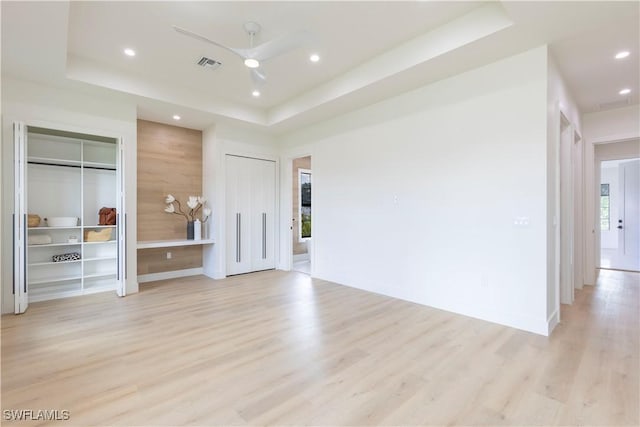 unfurnished living room with light hardwood / wood-style flooring, a raised ceiling, and ceiling fan