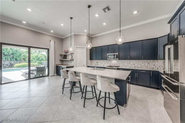 kitchen with sink, backsplash, hanging light fixtures, stainless steel appliances, and a center island with sink