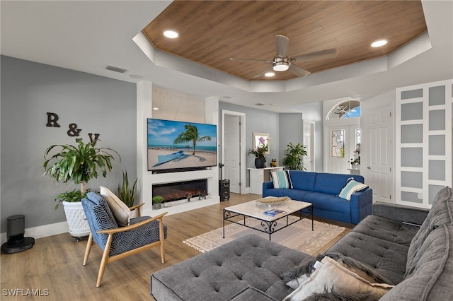 living room with a raised ceiling, a large fireplace, wood ceiling, and light hardwood / wood-style floors