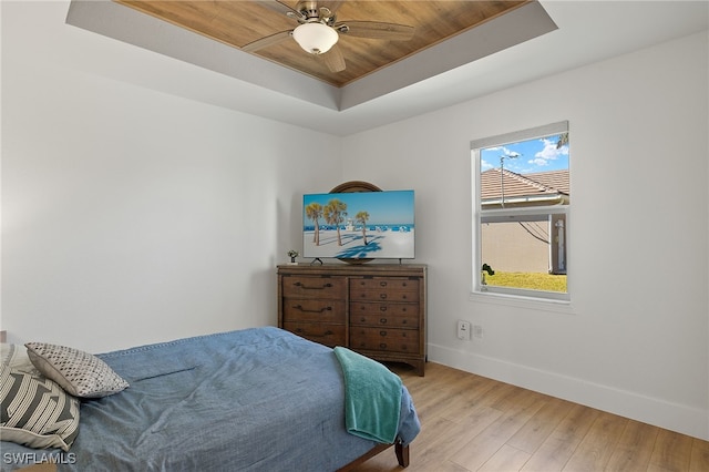 bedroom with light wood-type flooring, baseboards, a tray ceiling, and a ceiling fan