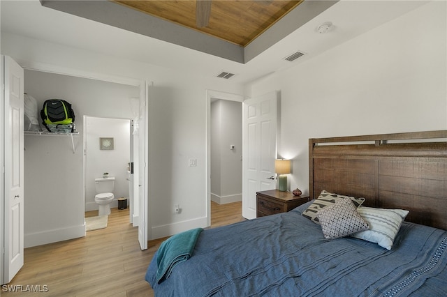 bedroom with wood ceiling, light hardwood / wood-style flooring, a raised ceiling, and ensuite bathroom