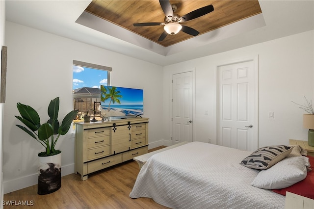 bedroom with light wood-style flooring, a tray ceiling, ceiling fan, and baseboards