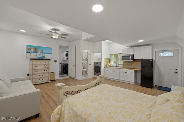 bedroom with connected bathroom, sink, black fridge, light wood-type flooring, and washer / clothes dryer