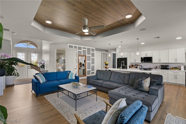 living area featuring light wood-style floors, a tray ceiling, wooden ceiling, and visible vents