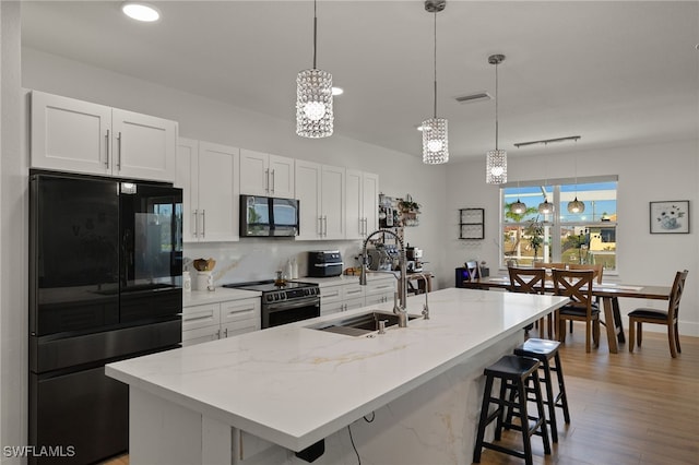 kitchen with black appliances, a kitchen island with sink, white cabinets, and decorative light fixtures