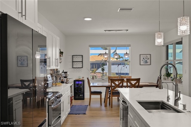 kitchen featuring white cabinets, stainless steel appliances, light wood-type flooring, pendant lighting, and a sink