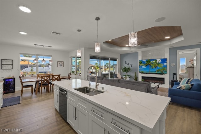 kitchen featuring sink, white cabinetry, a kitchen island with sink, black dishwasher, and a raised ceiling