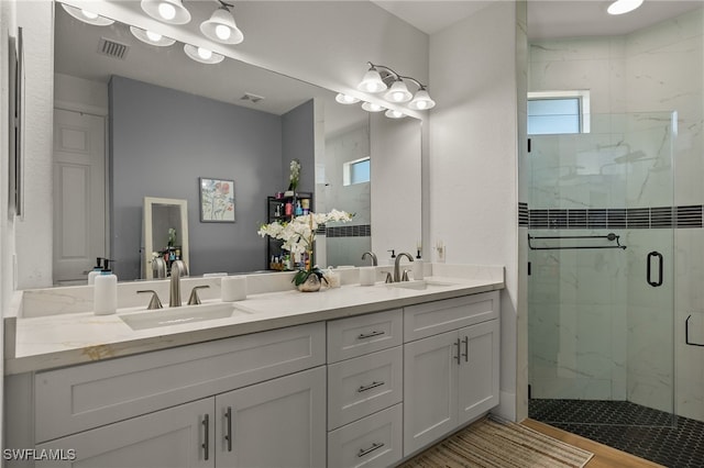 full bath with a sink, double vanity, a marble finish shower, and visible vents