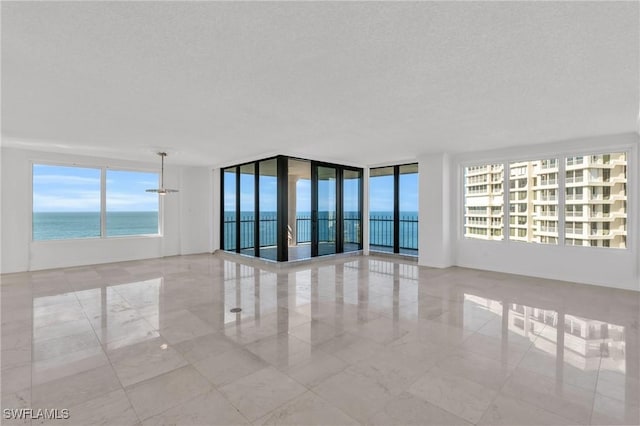 empty room with a water view, a textured ceiling, and a wall of windows