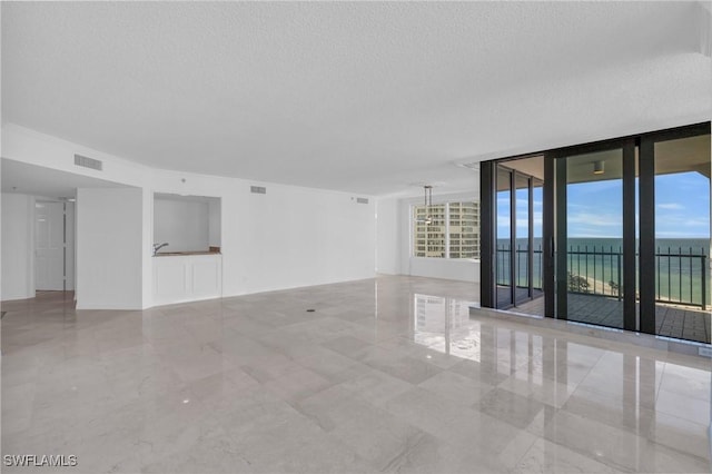 empty room featuring a water view, floor to ceiling windows, and a textured ceiling