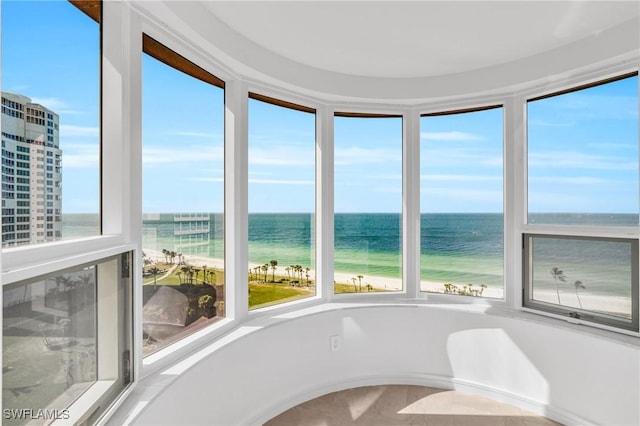 unfurnished sunroom featuring a water view, a healthy amount of sunlight, and a view of the beach