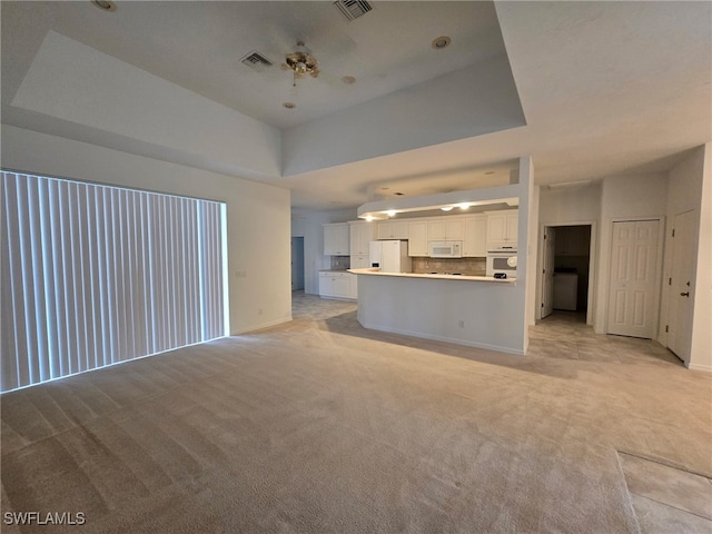 unfurnished living room featuring a raised ceiling and light colored carpet