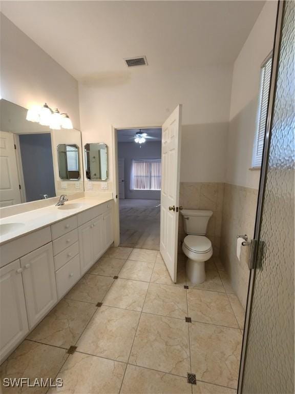 bathroom with tile walls, vanity, ceiling fan, toilet, and tile patterned floors