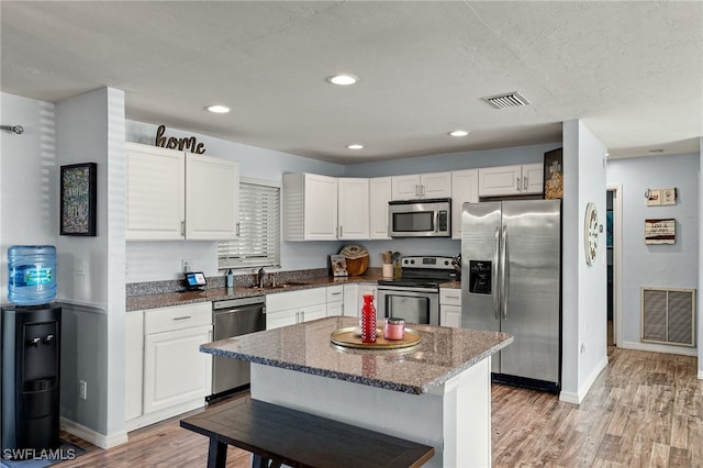 kitchen featuring appliances with stainless steel finishes, dark stone countertops, white cabinets, a center island, and light hardwood / wood-style flooring