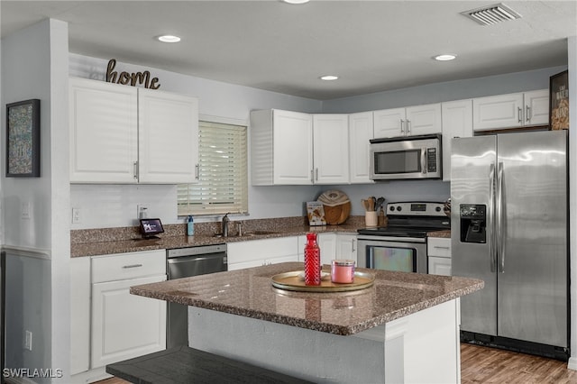 kitchen with sink, white cabinetry, stainless steel appliances, light hardwood / wood-style floors, and a kitchen island